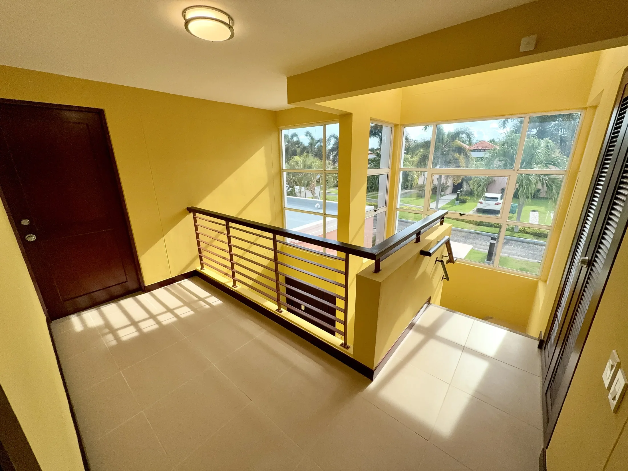Upper-level landing with yellow walls, metal railing, dark wood door, and large windows