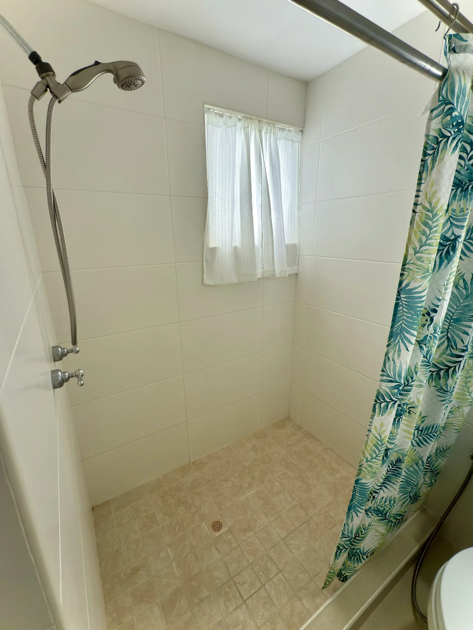 Walk-in shower with tropical leaf curtain, handheld showerhead, and small window