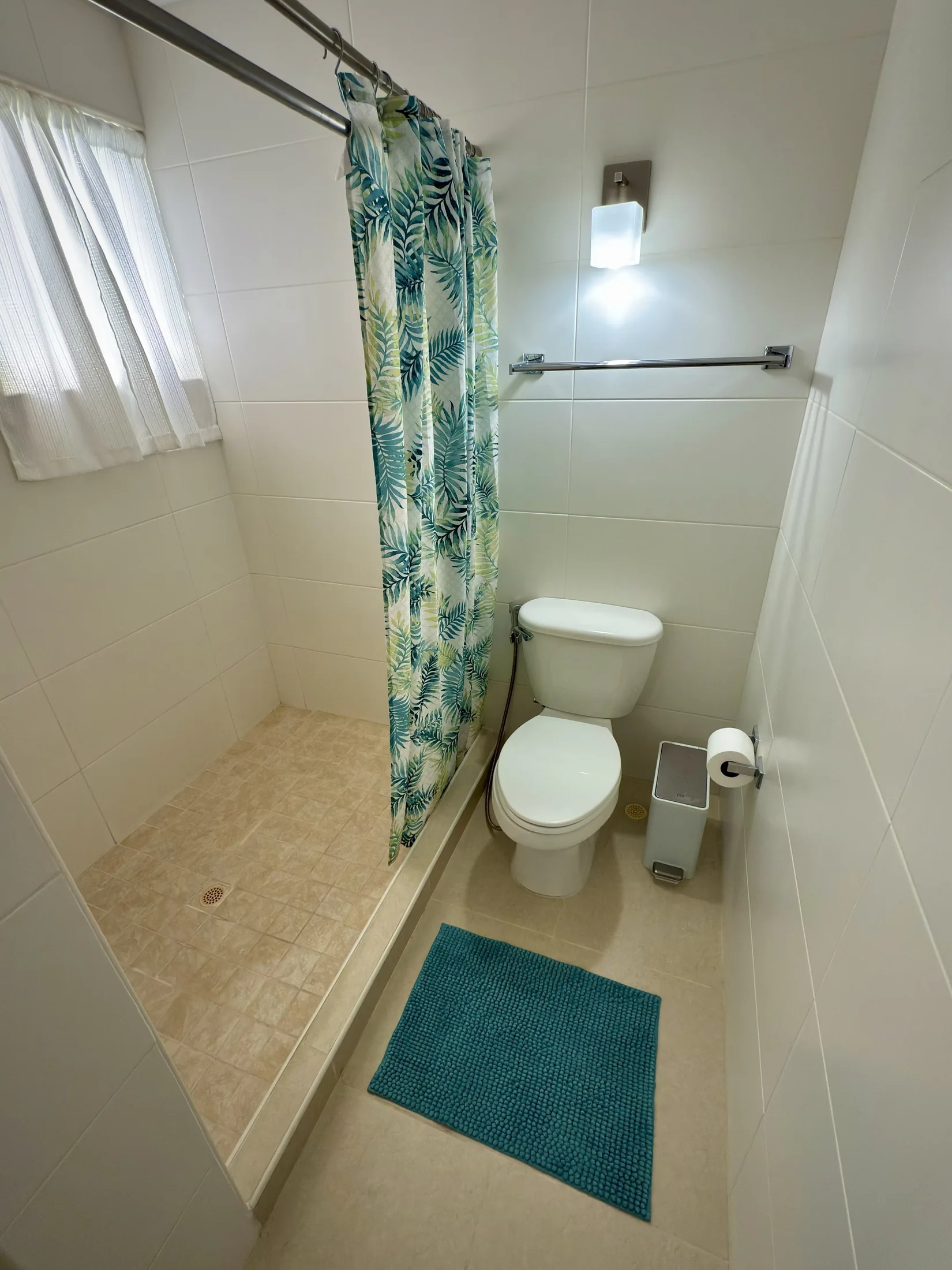 Bathroom with tropical leaf shower curtain, toilet, and teal bath mat