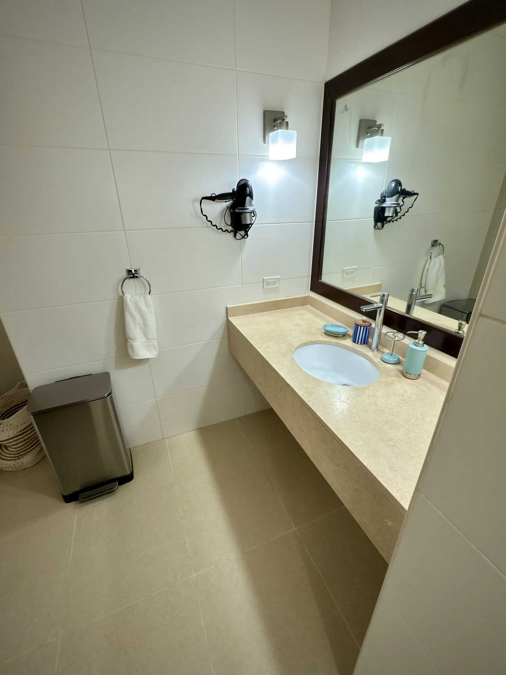 Stone countertop vanity with dark-framed mirror, wall sconces, and hair dryer