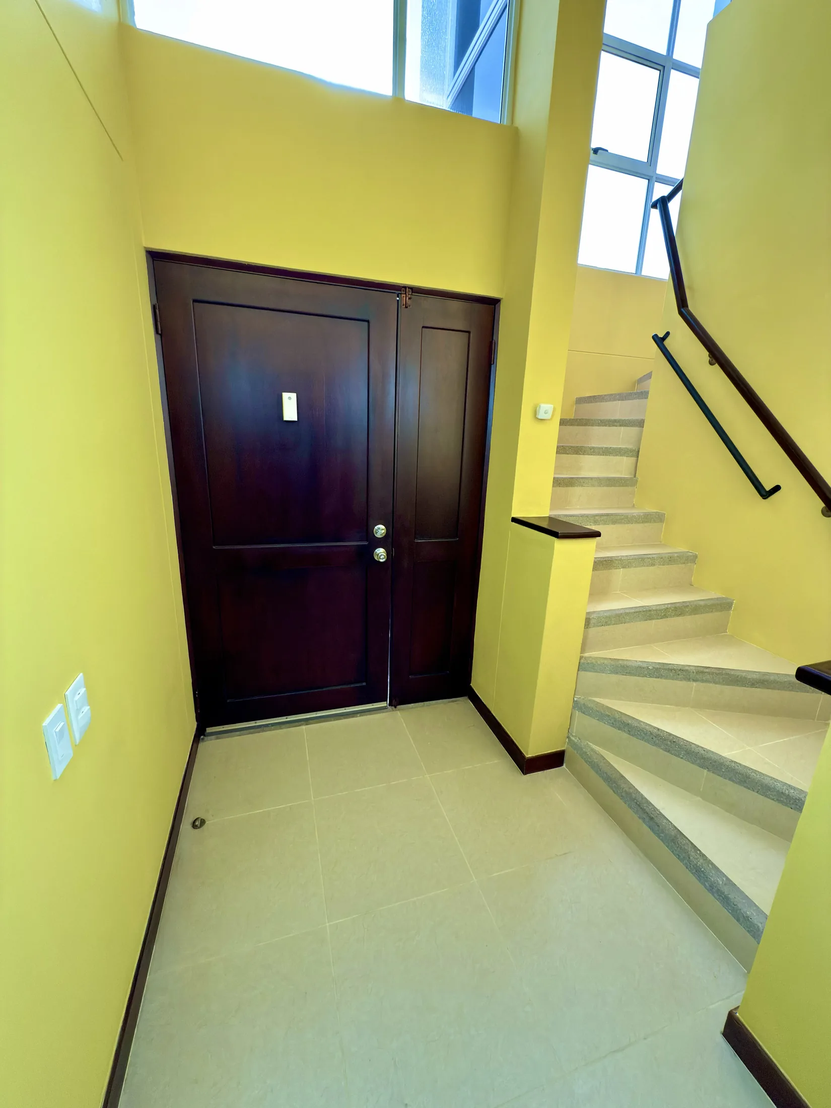 Entry foyer with dark wood double doors, yellow walls, and staircase