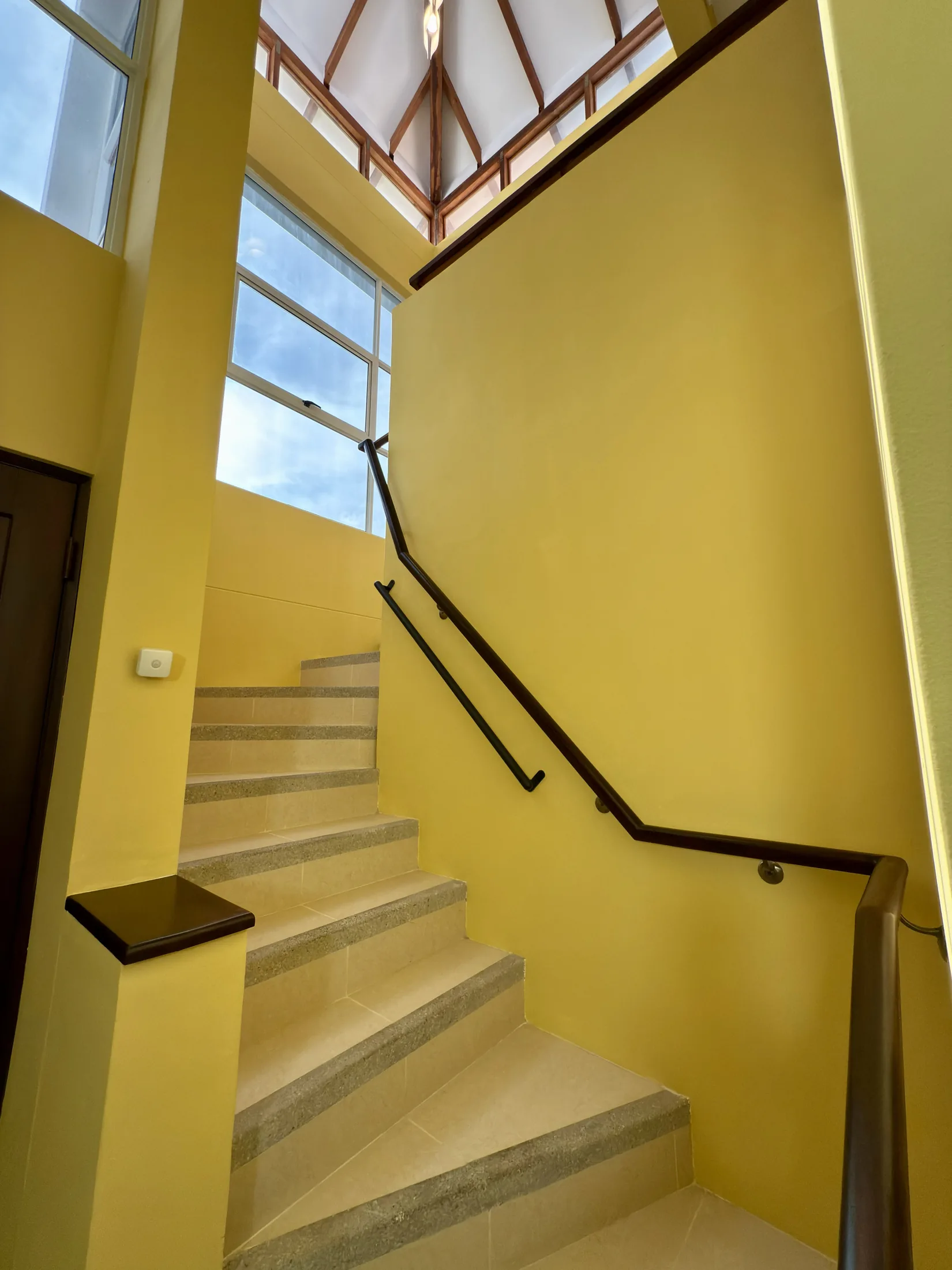 Yellow-walled stairway with metal handrails and vaulted wood-beam ceiling above