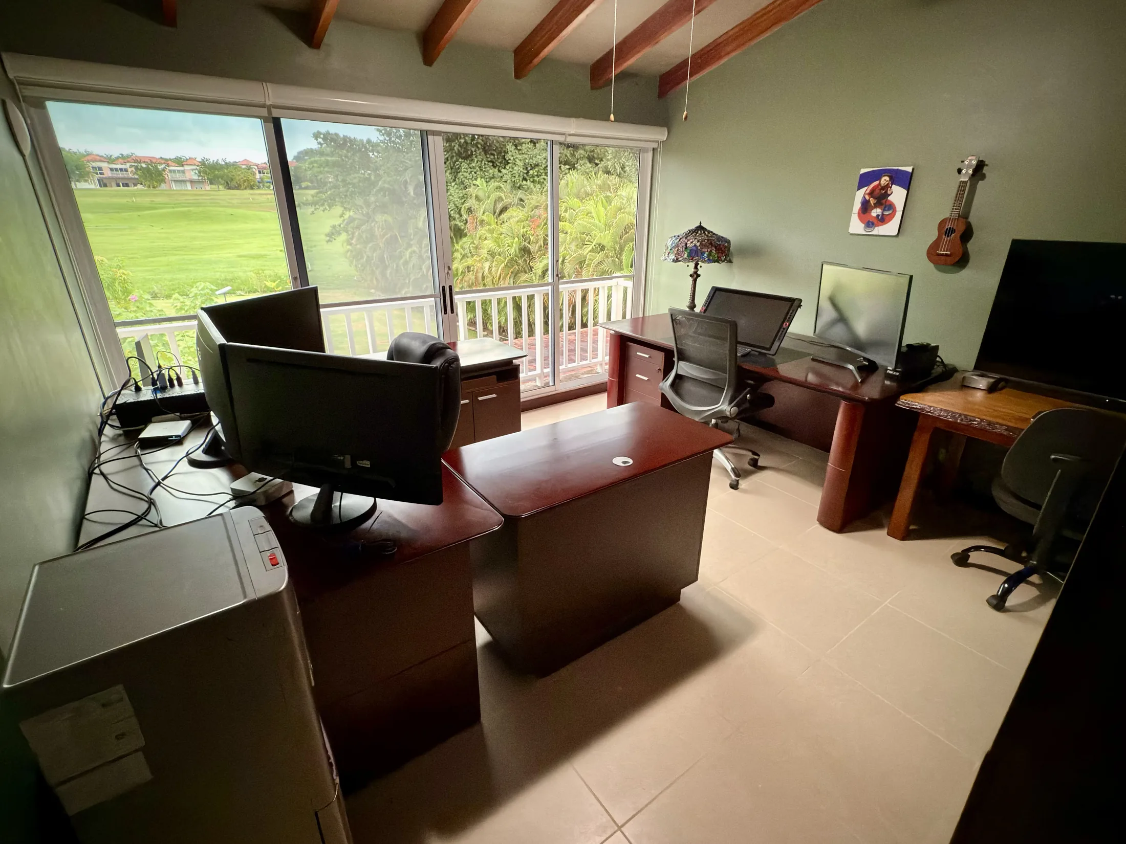 Office with dual desks, monitors, guitar on wall, and golf-course view through sliding doors