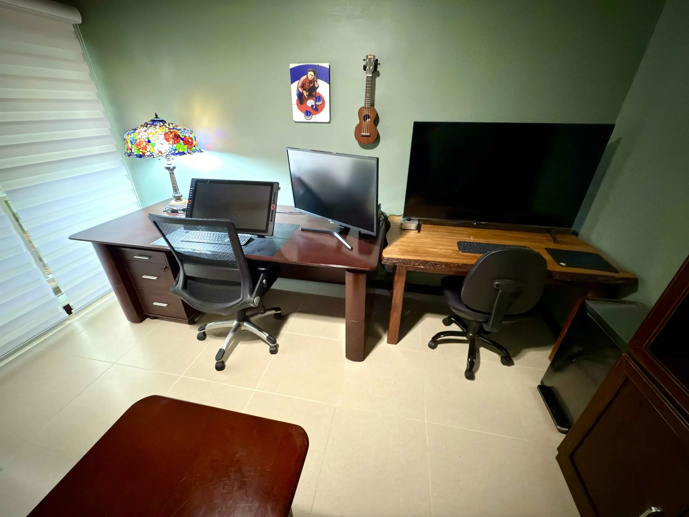 Office side angle with dual desks, monitors, Tiffany lamp, and ukulele on wall