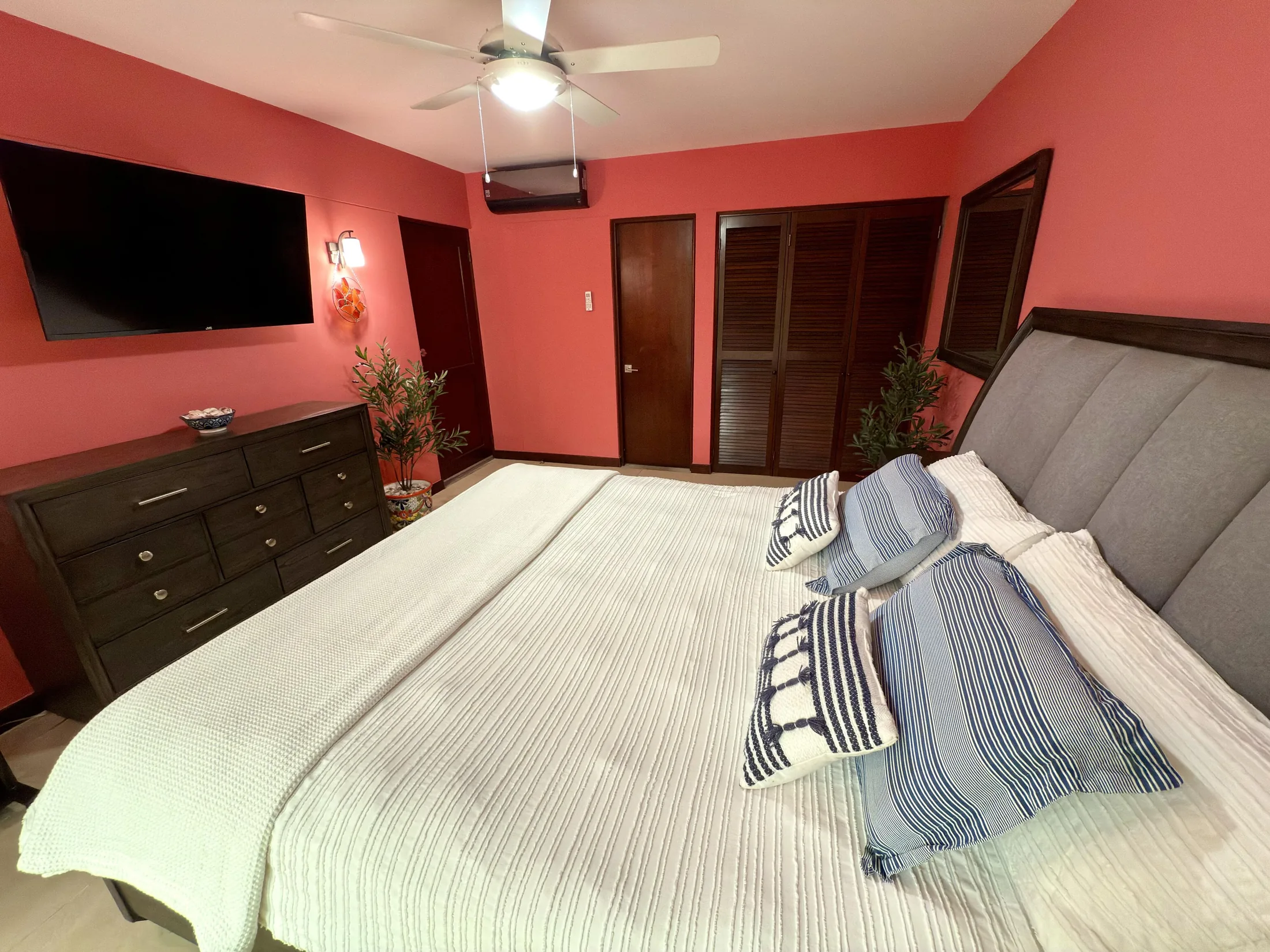 Coral bedroom showing wall-mounted TV, dark dresser, and closet doors