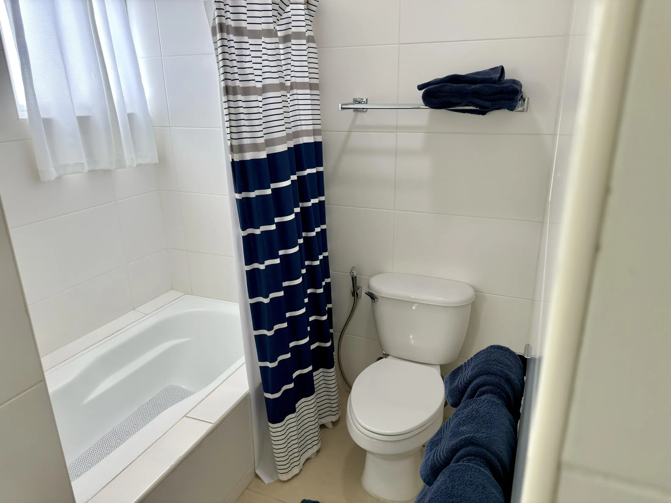 Bathroom with bathtub, striped navy-and-white shower curtain, toilet, and blue towels