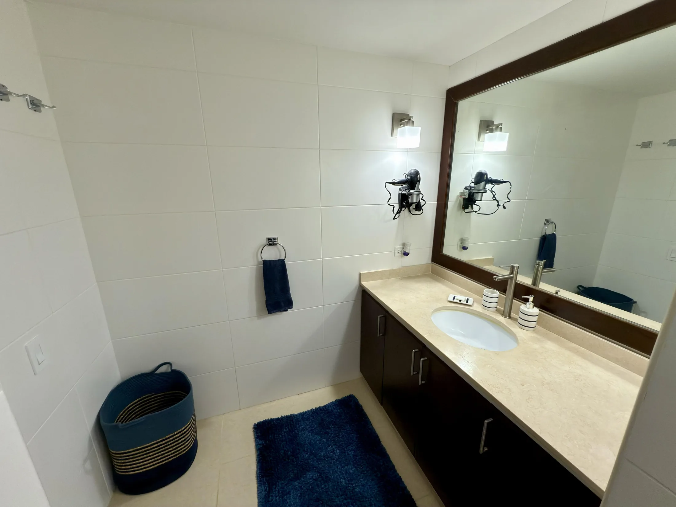 Bathroom vanity with dark wood cabinet, stone countertop, navy bath mat, and wood-framed mirror