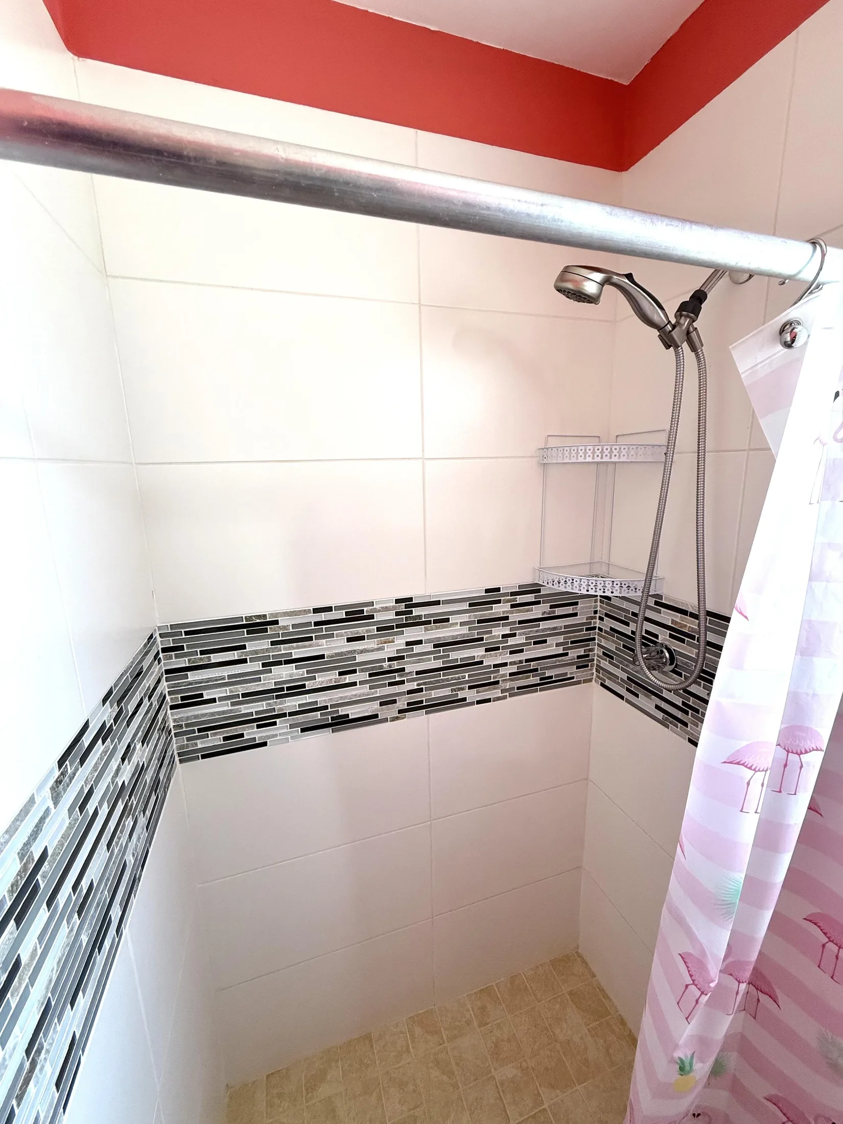 Shower with mosaic tile accent strip, coral-red ceiling, and flamingo-patterned curtain