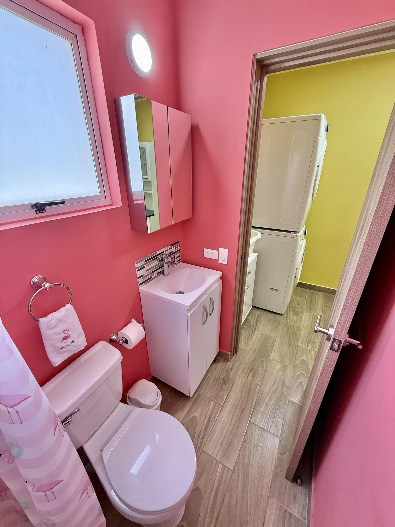 Small pink half-bath with toilet, white vanity, and mirror cabinet next to laundry area