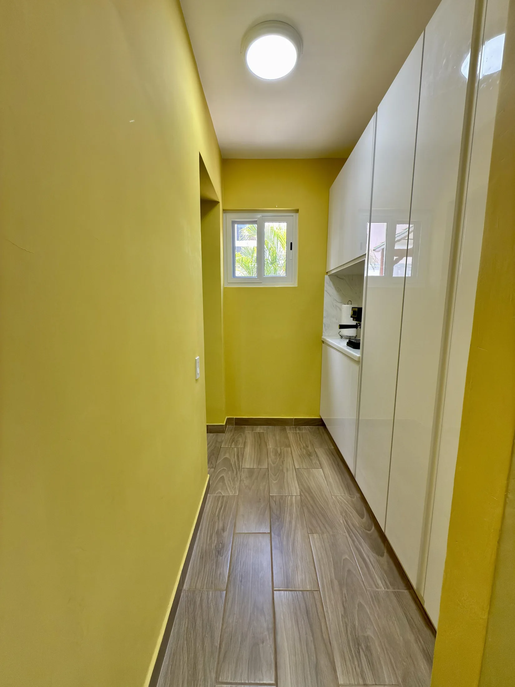 Long pantry corridor with yellow walls, white cabinets, and window at far end
