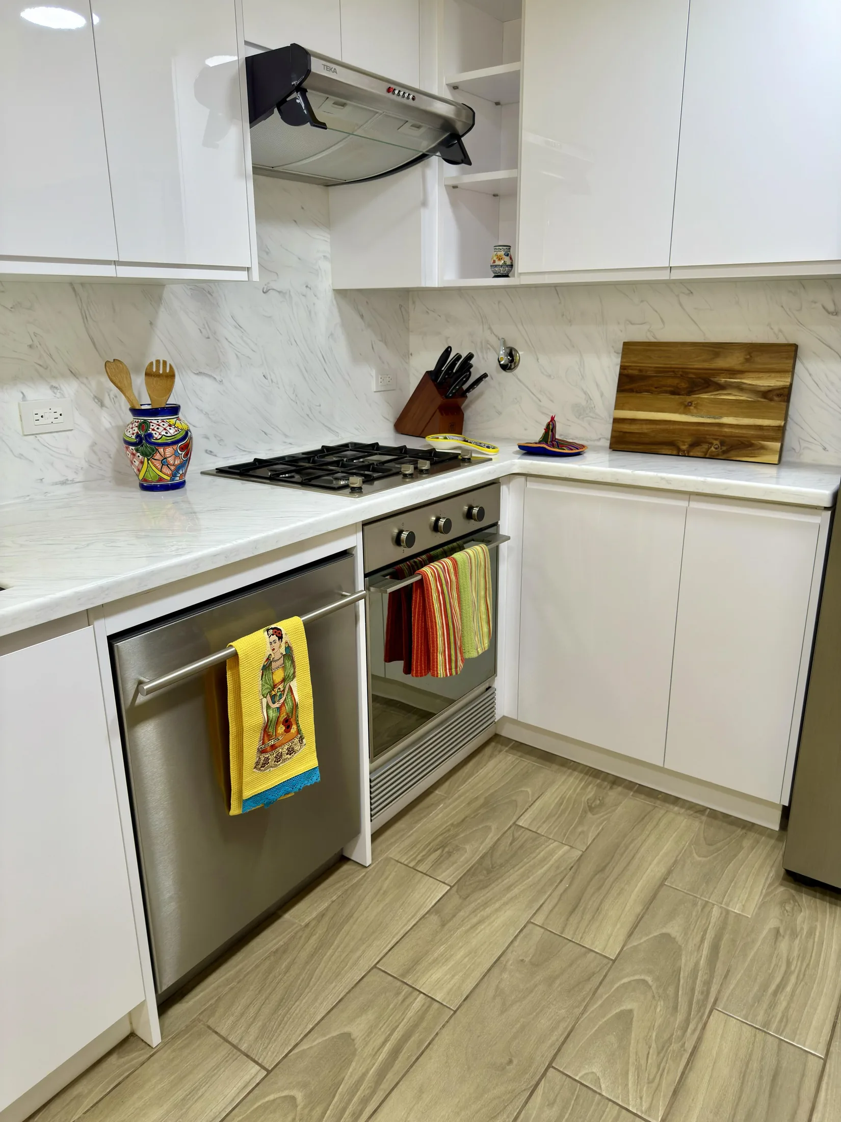 Kitchen gas cooktop with range hood, marble backsplash, knife block, and colorful towels