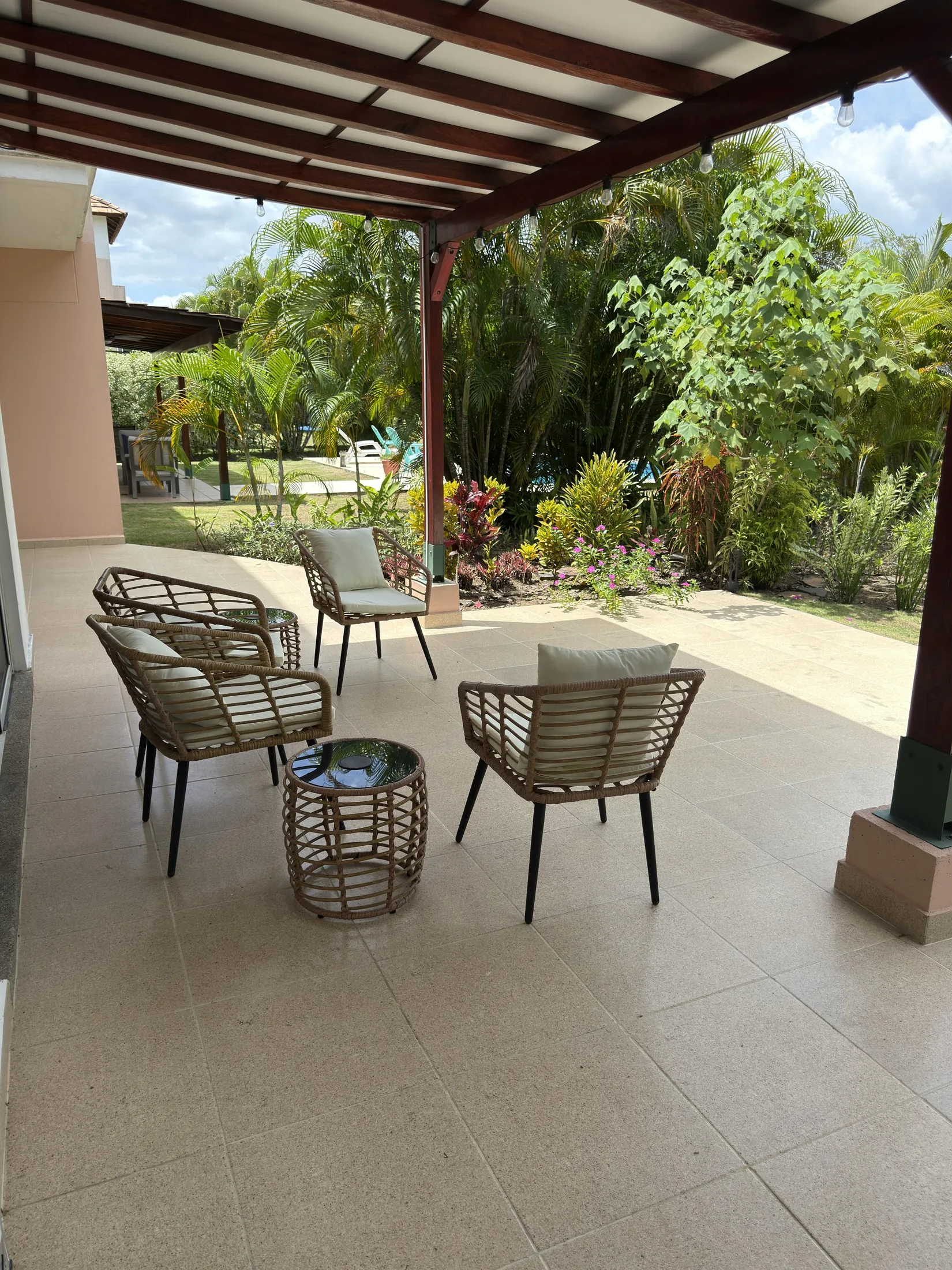 Covered patio with wicker chairs, cushions, and tropical garden
