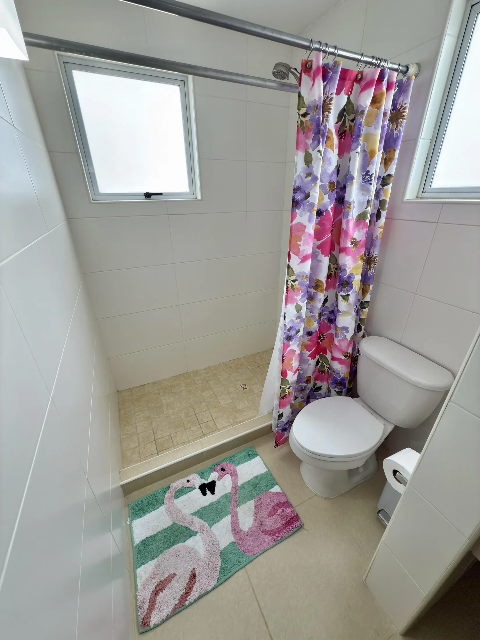 Bathroom with colorful floral shower curtain, flamingo bath mat, and toilet